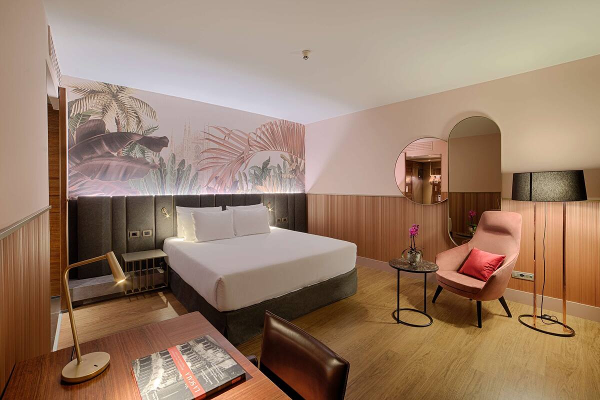 Una habitación de hotel con cama, escritorio, silla, mesita y espejo.