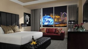 Habitación de hotel con una cama grande, un sofá rojo, un reposapiés negro y vistas a un paisaje urbano con una noria.