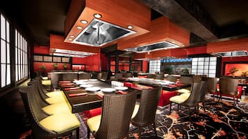 A modern restaurant with high ceilings, exposed beams, and a central dining area with long tables and wicker chairs.