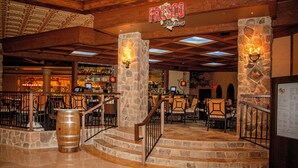 Una zona de bar con pilares de piedra, taburetes de madera y un barril de madera.