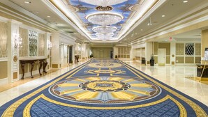 Un amplio pasillo con alfombra de diseño azul y dorado, detalles ornamentales en el techo y candelabros.