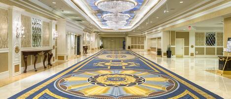 A grand hallway with a blue and gold patterned carpet, ornate ceiling design, and chandeliers.