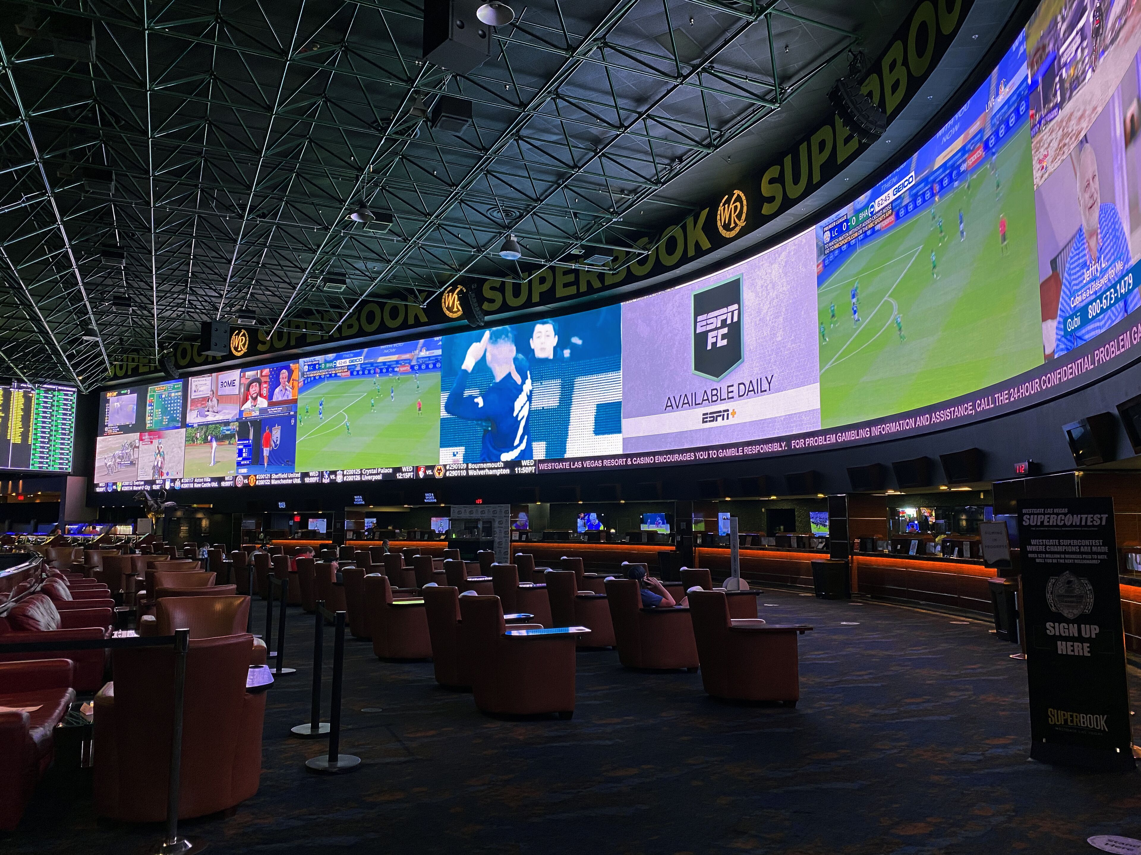 A large indoor sports arena with multiple screens displaying sports events, seating areas, and a prominent sign for the Westgate SuperBook.