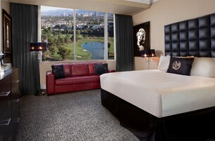 A hotel room with a large bed, a red leather sofa, a view of a golf course, and a cityscape.