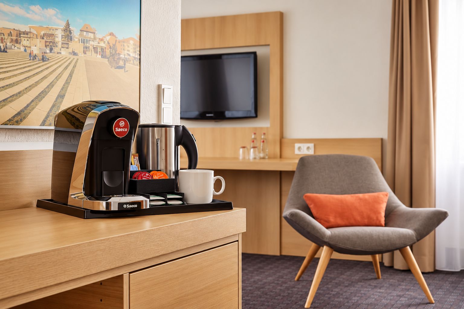 Une chambre d’hôtel équipée d’une machine à café, d’une tasse, d’une chaise, d’un téléviseur et d’une fenêtre avec des rideaux.