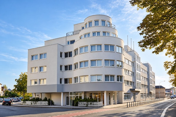 A multi-story hotel with a curved facade, large windows, and a white fence in front.