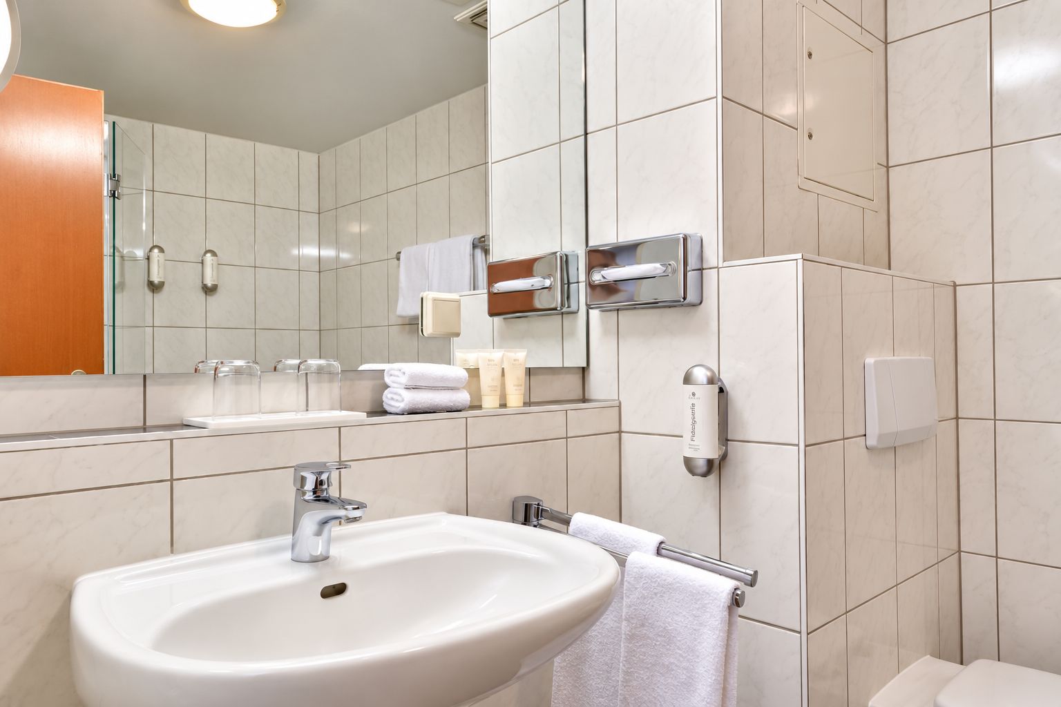 A modern bathroom with a sink, mirror, towel rack, and toiletries.