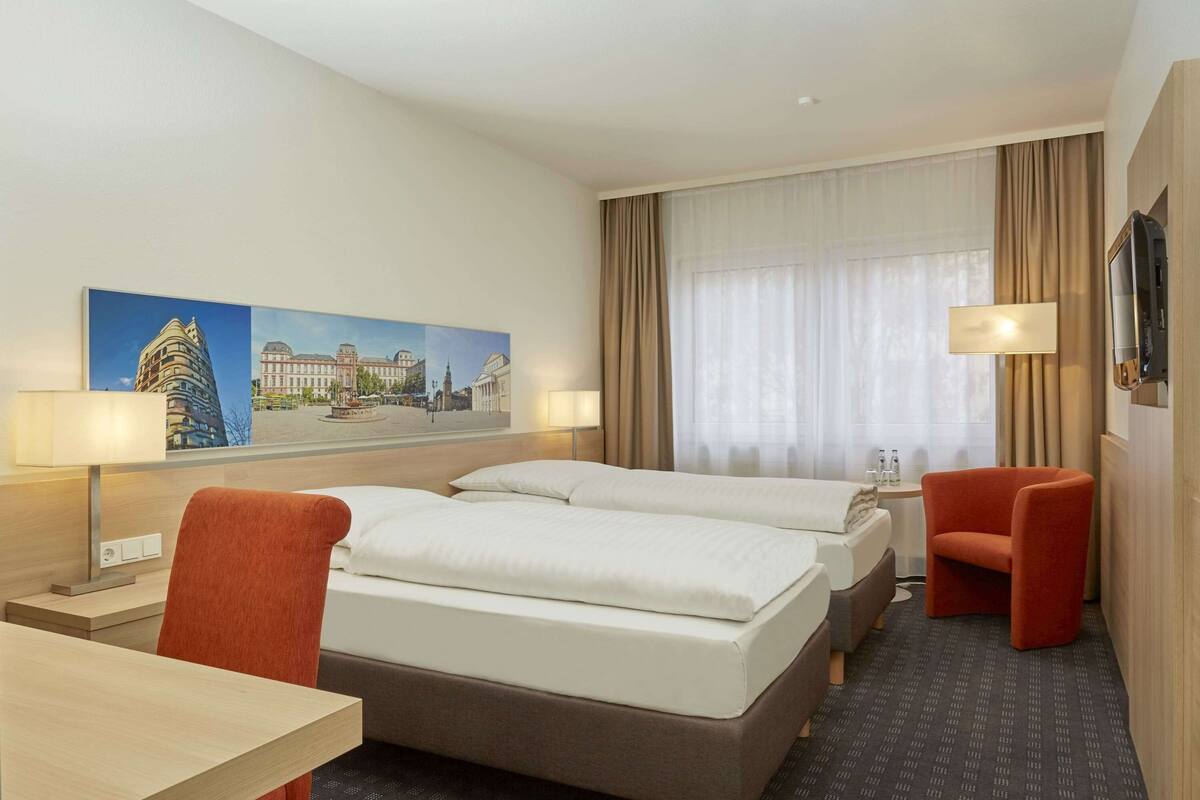 Une chambre d’hôtel avec deux lits, un bureau, une chaise, une télévision et un tableau au mur.