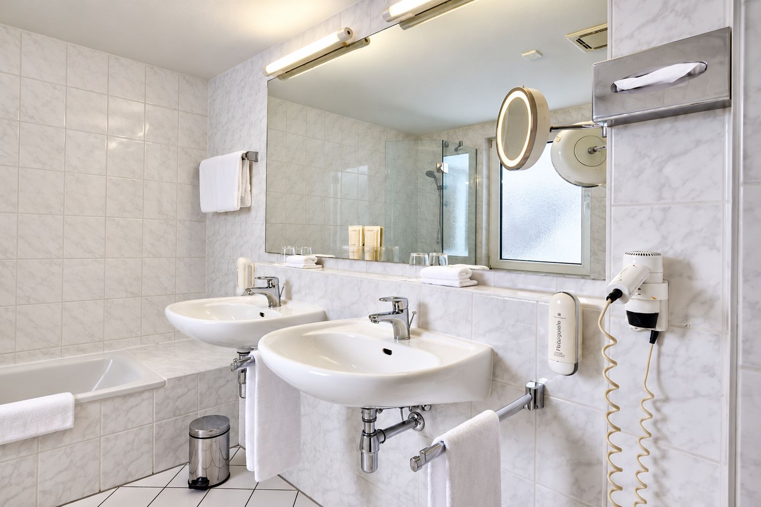 Un baño moderno con dos lavamanos, un espejo grande, un secador de pelo y un perchero para toallas.