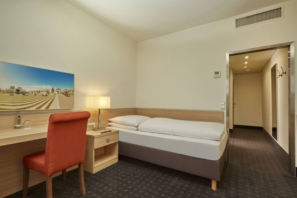 Une chambre d’hôtel avec un lit, un bureau et une chaise, une lampe et un tableau au mur.