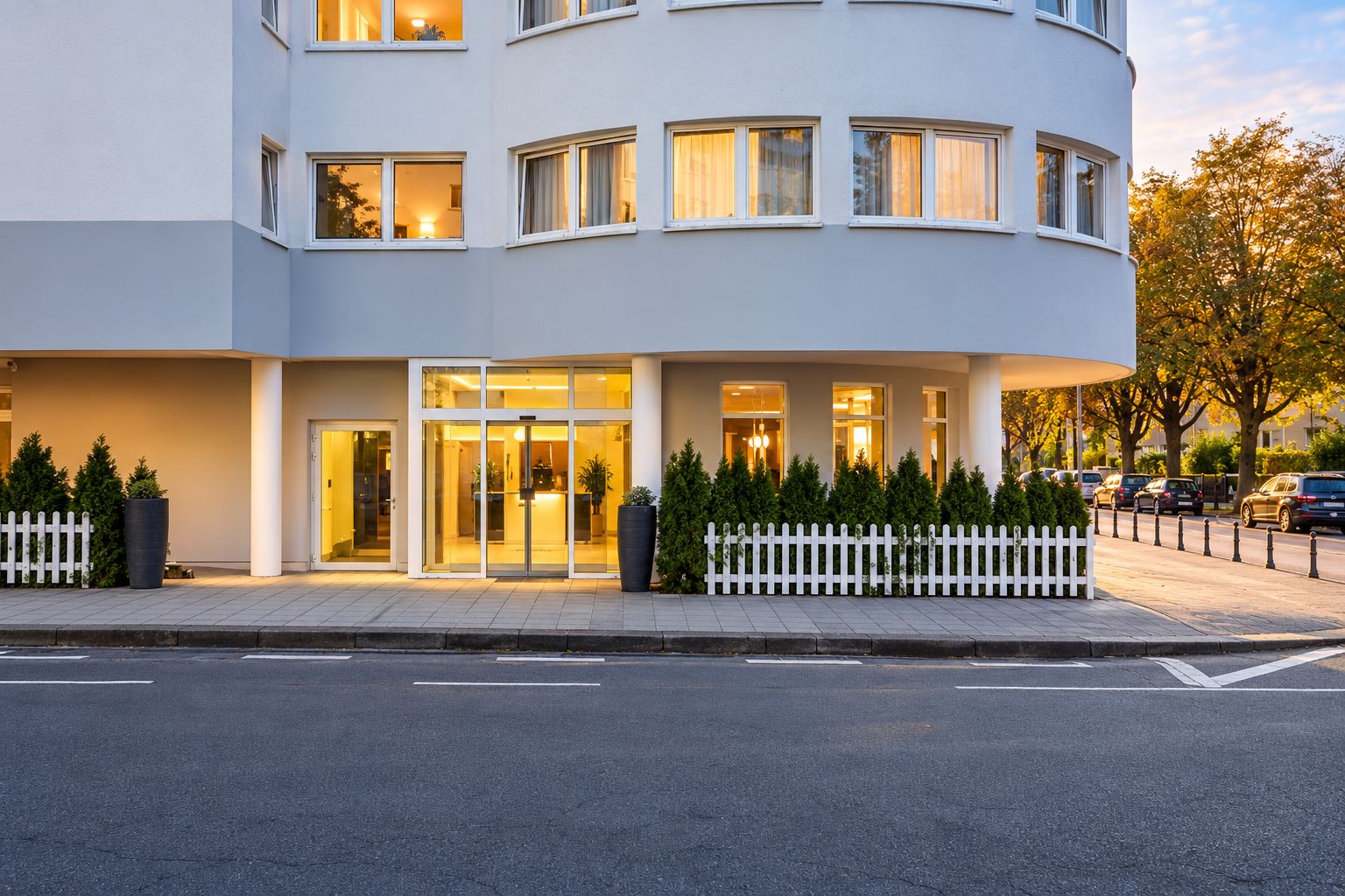 Ein modernes Hotel mit geschwungener Fassade, großem Glas Eingang und weißem Zaun.