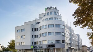 A modern H+Hotel building with a curved facade, multiple windows, and a prominent sign.