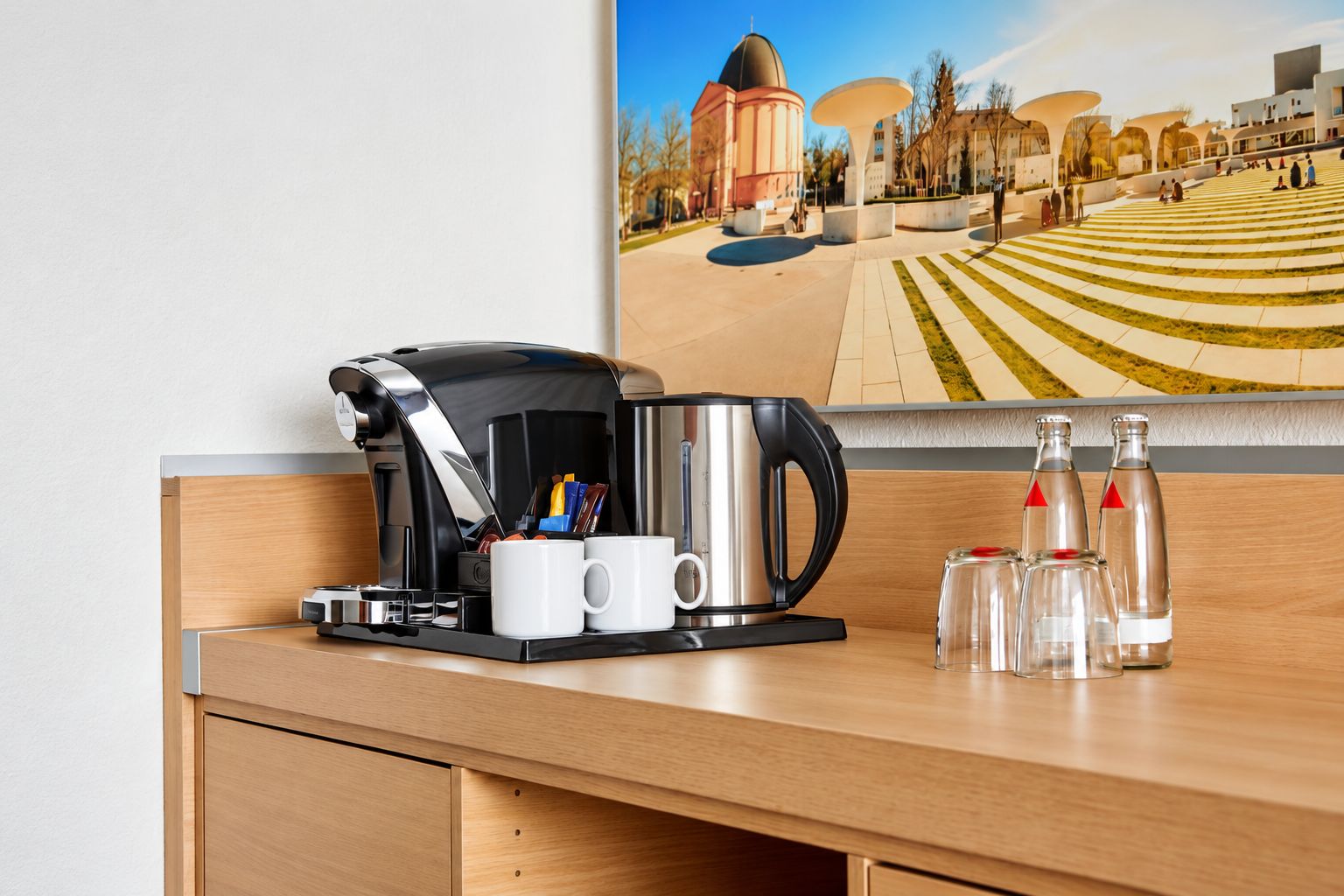 Habitación de hotel con cafetera, dos tazas y dos botellas de agua sobre la encimera.