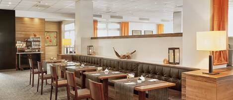 A restaurant with wooden tables and chairs, a cushioned bench, and a counter with a lamp.