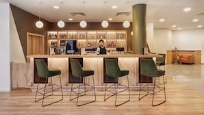 A bar area with a wooden counter, green bar stools, and a bartender.