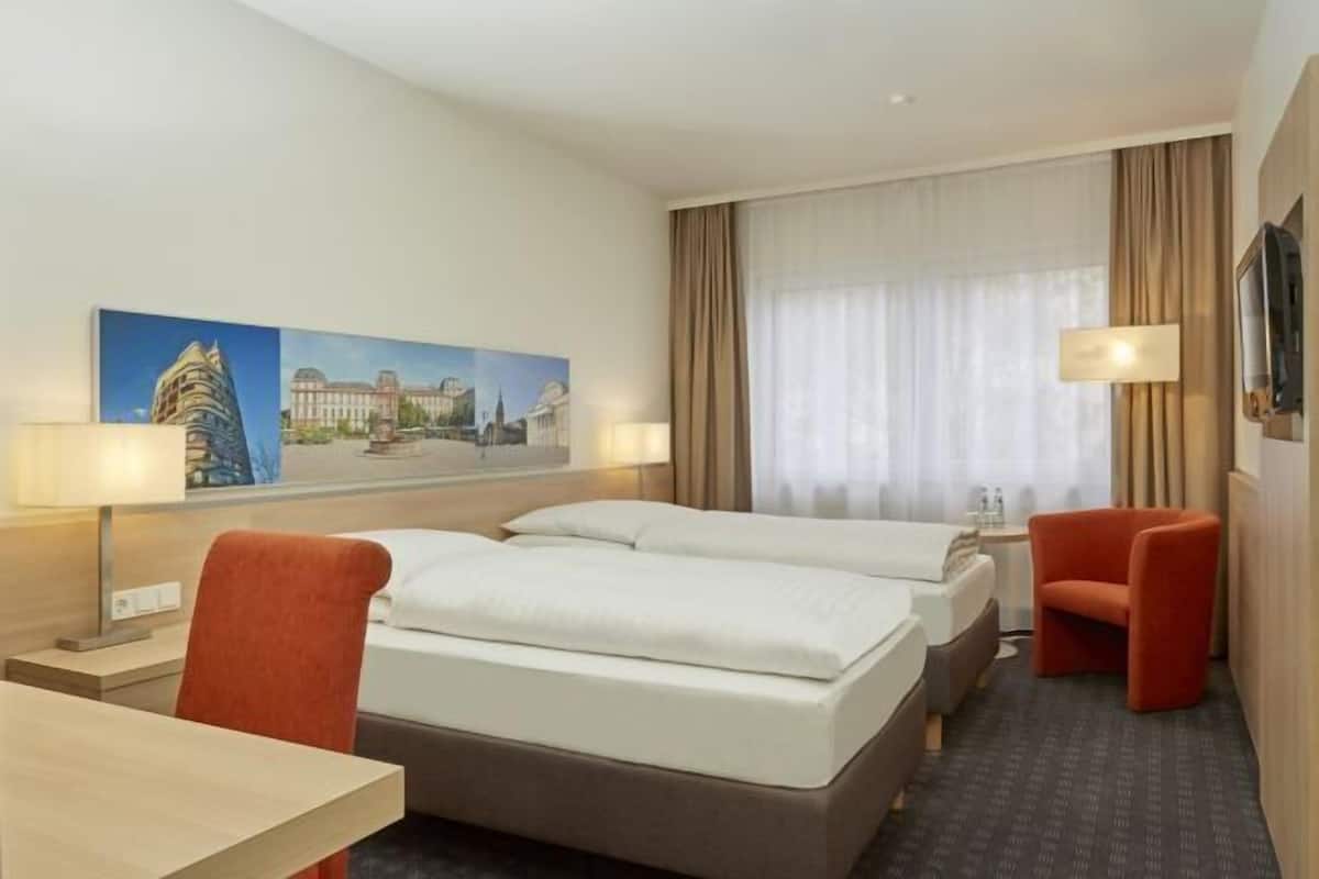 Une chambre d’hôtel avec deux lits, un bureau, une chaise, une télévision et un tableau au mur.