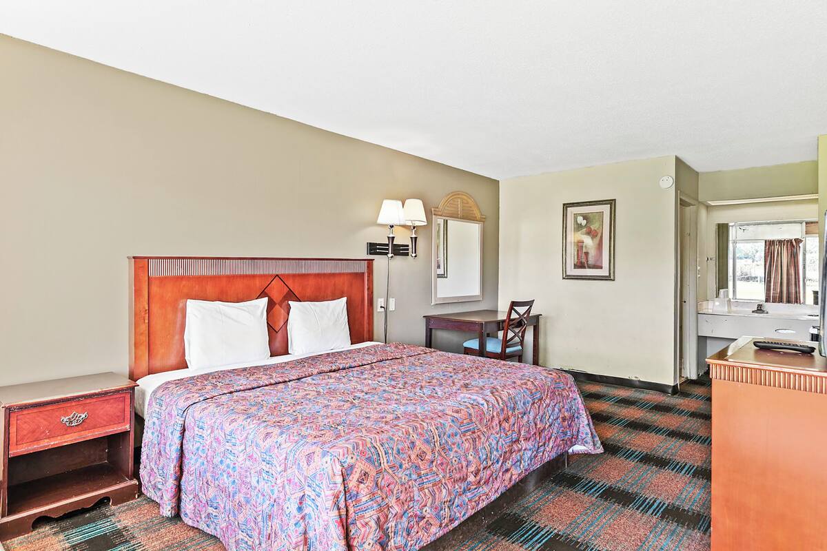 Une chambre d’hôtel comprenant un lit, une table de chevet, un bureau, une chaise et une salle de bain avec un miroir et un lavabo.