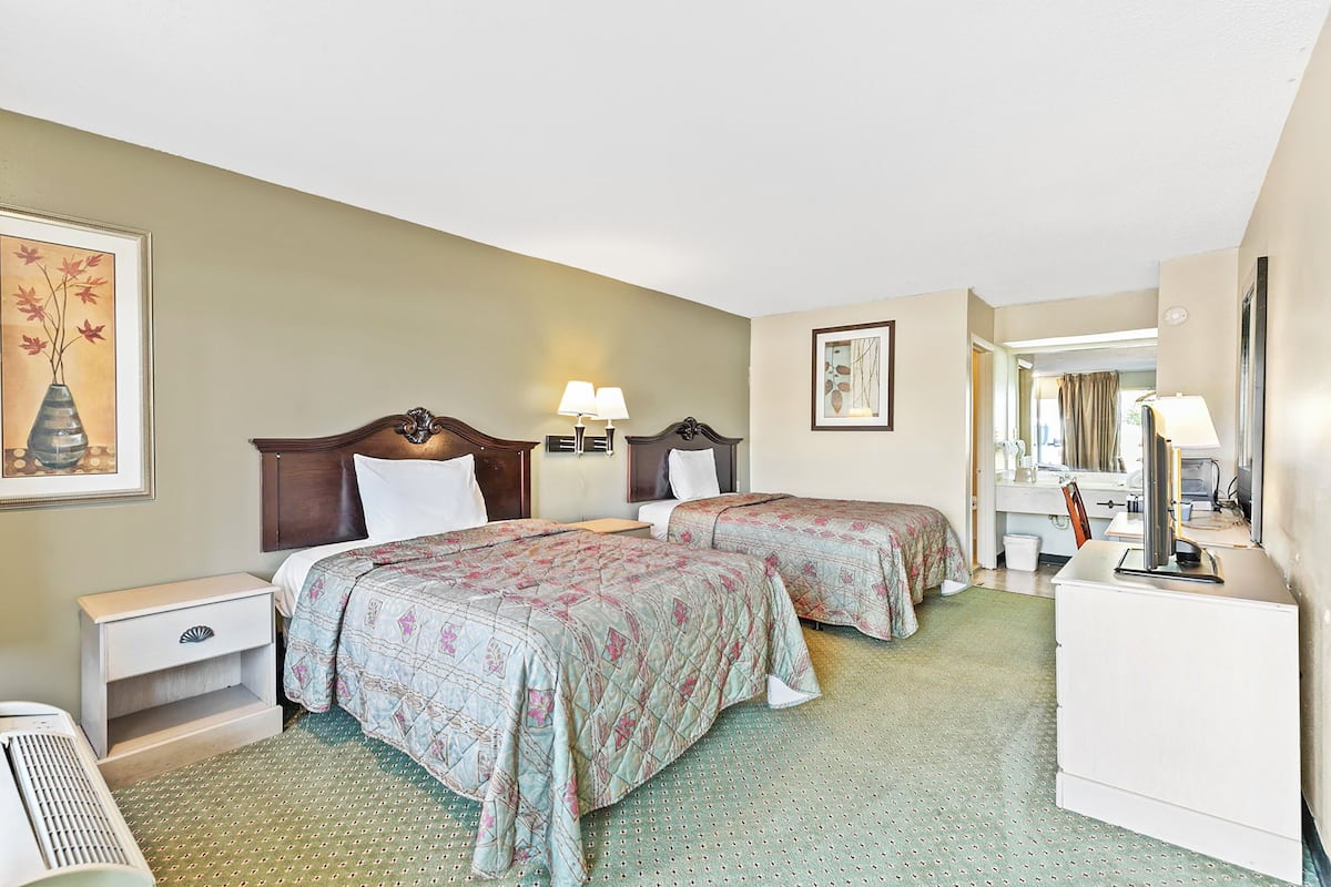 Une chambre d’hôtel avec deux lits, un bureau, une chaise, une commode et un miroir.