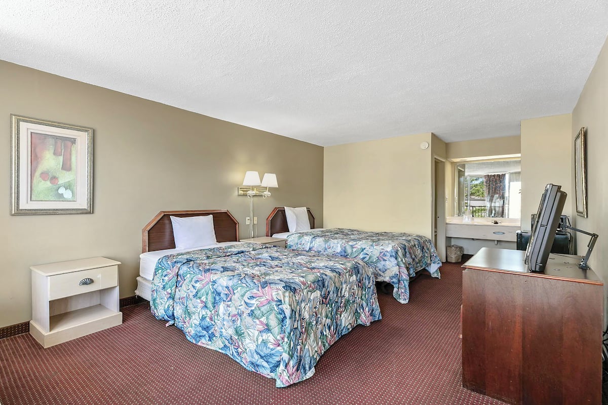 Une chambre d’hôtel avec deux lits, une table de chevet, un bureau, un miroir et une fenêtre.