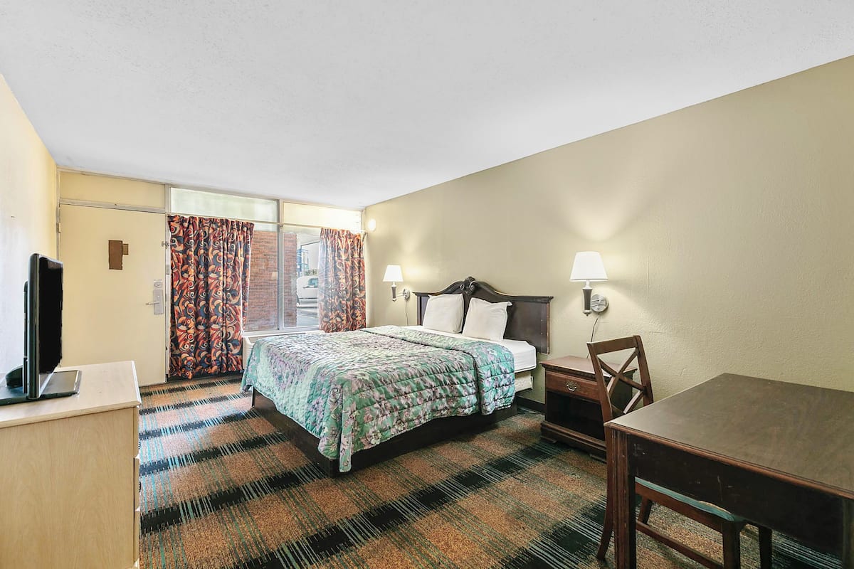 Une chambre d’hôtel avec un lit, un bureau, une chaise, une télévision et une fenêtre avec des rideaux.