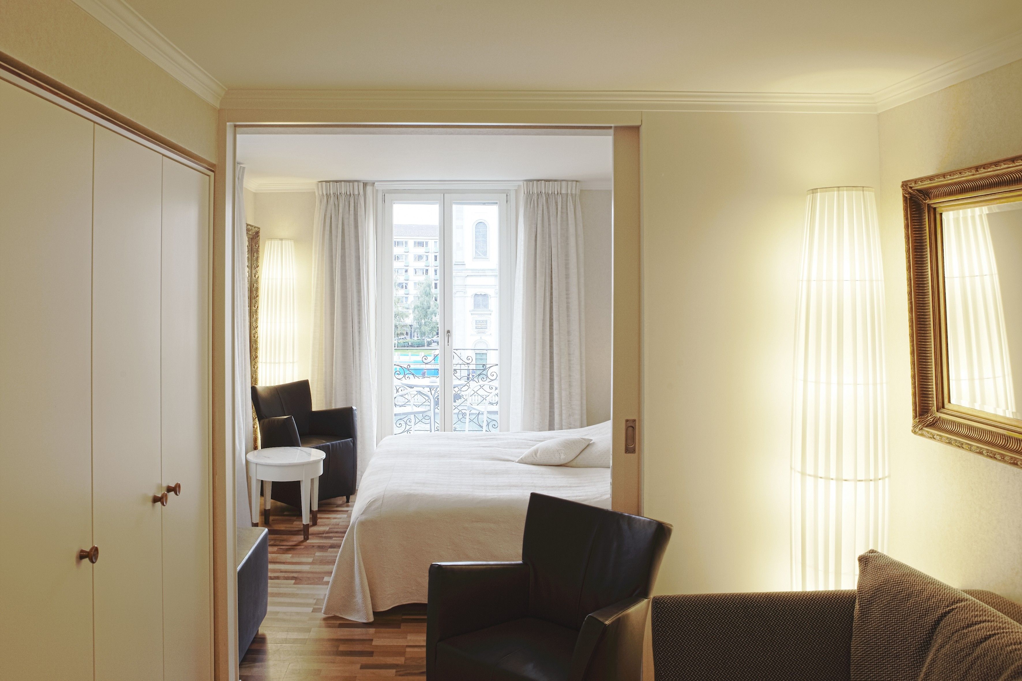 Una habitación de hotel con una cama, una silla, una mesita y una ventana con cortinas.
