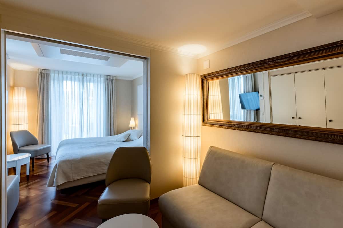 Une chambre d’hôtel avec un lit, un canapé, une chaise, une lampe et un téléviseur.