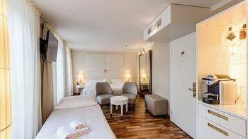 A hotel room with a bed, two chairs, a small table, a minibar, and a television.
