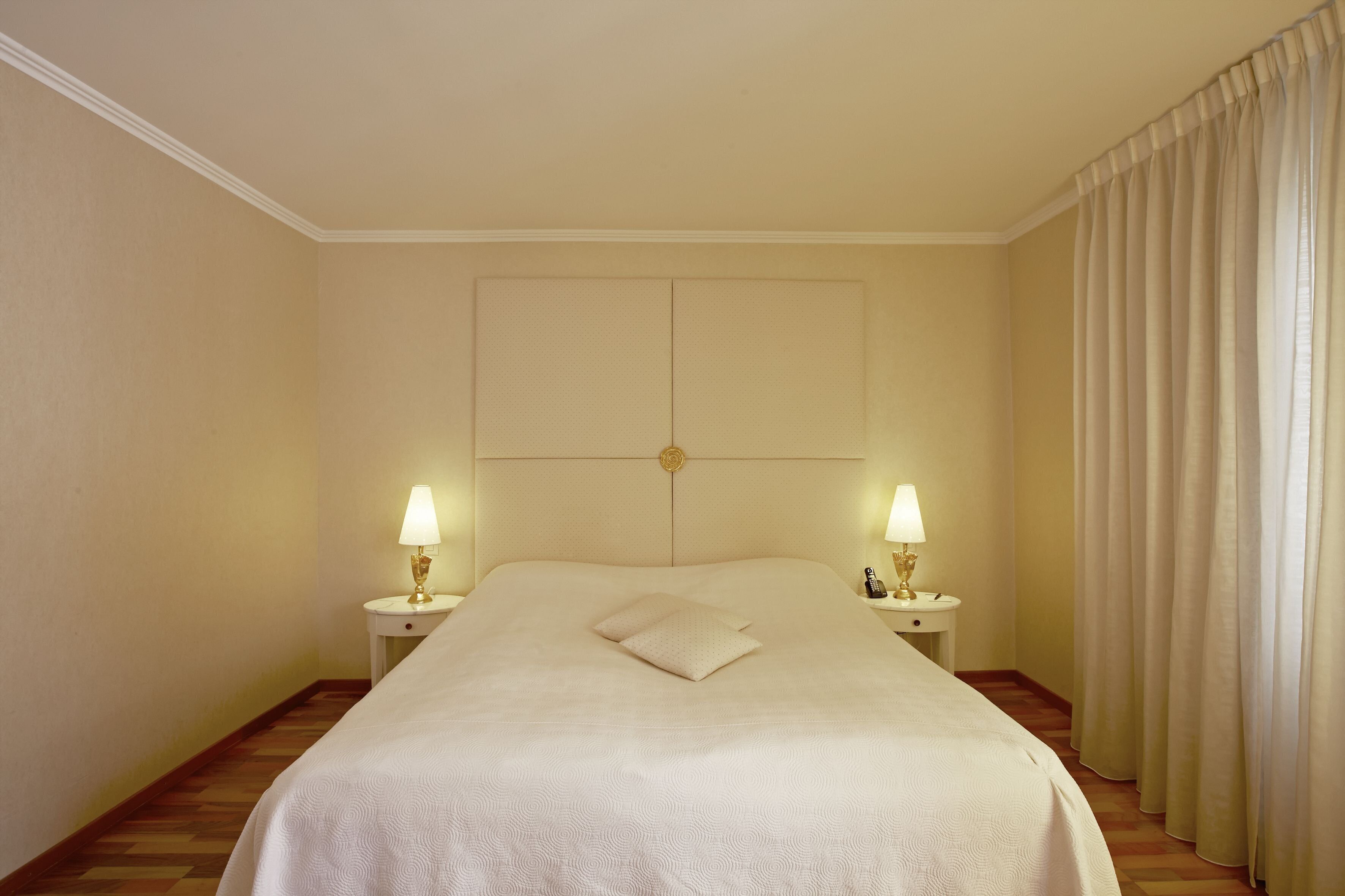 Une chambre d’hôtel avec un grand lit, deux lampes de chevet, une tête de lit et un rideau.