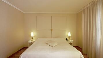 A hotel room with a large bed, two bedside lamps, a headboard, and a curtain.