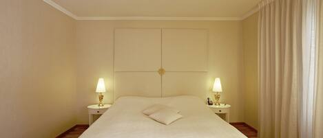 A hotel room with a large bed, two bedside lamps, a headboard, and a curtain.
