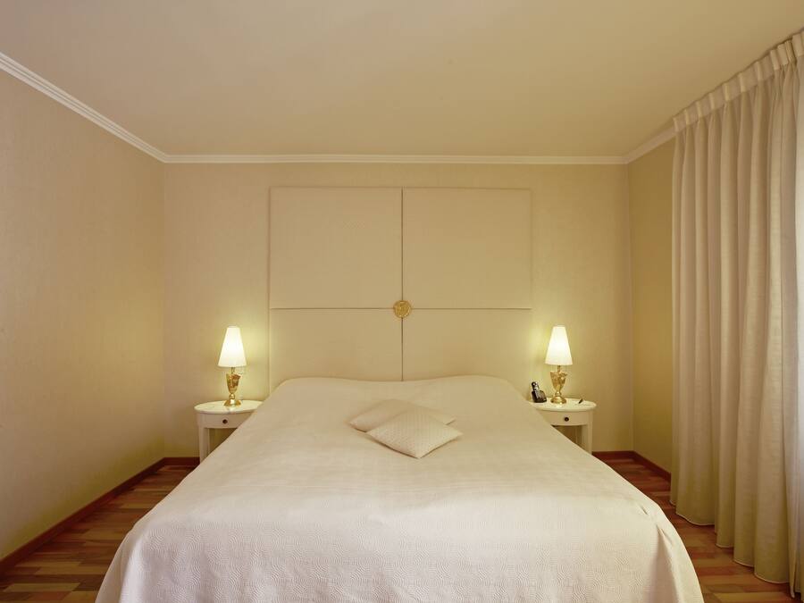 A hotel room with a large bed, two bedside lamps, a headboard, and a curtain.