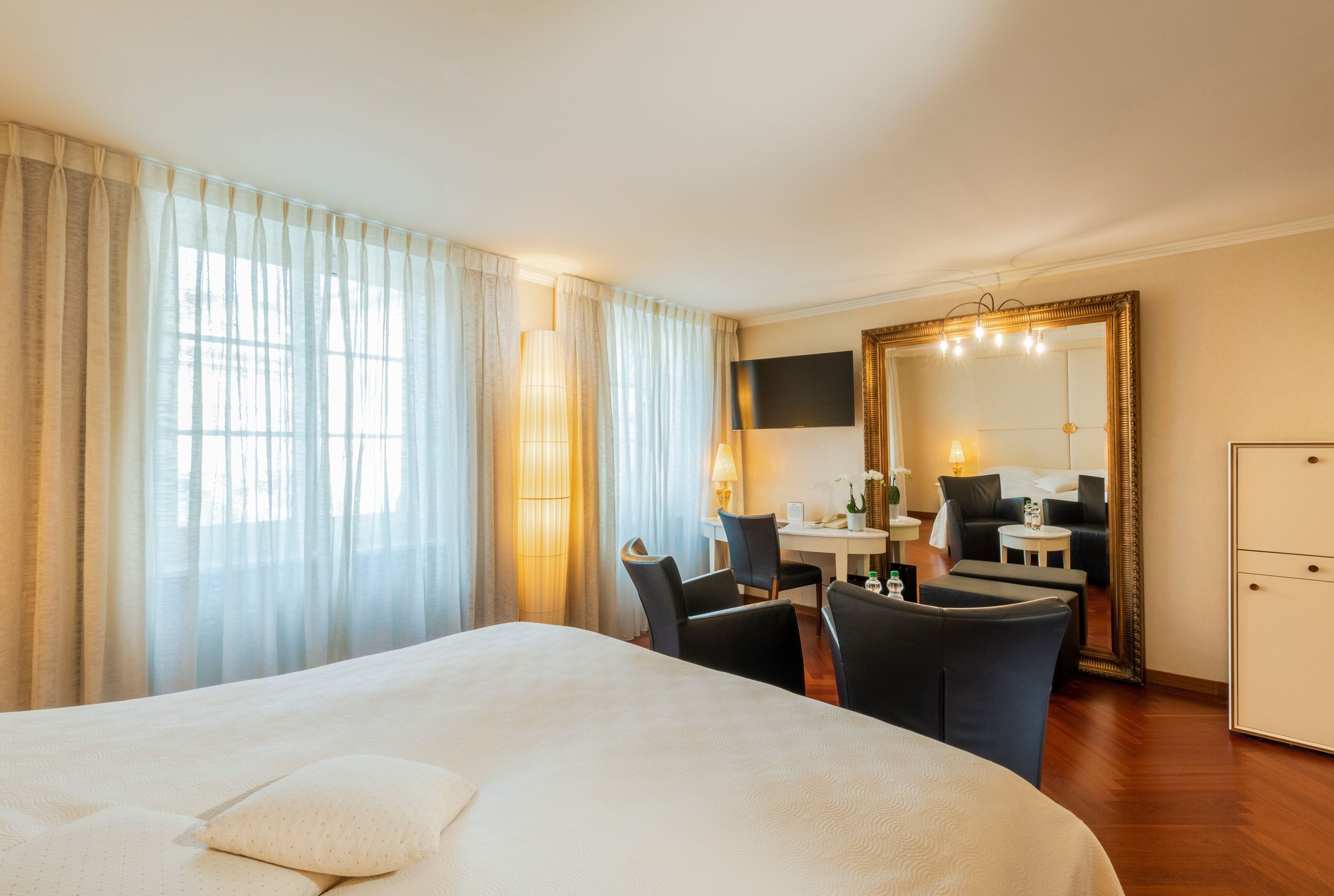 Ein Hotelzimmer mit einem großen Bett, einem Schreibtisch mit zwei Stühlen, einem Fernseher, einem Spiegel und einem Kleiderschrank.