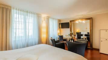 Ein Hotelzimmer mit einem großen Bett, einem Schreibtisch mit zwei Stühlen, einem Fernseher, einem Spiegel und einem Kleiderschrank.