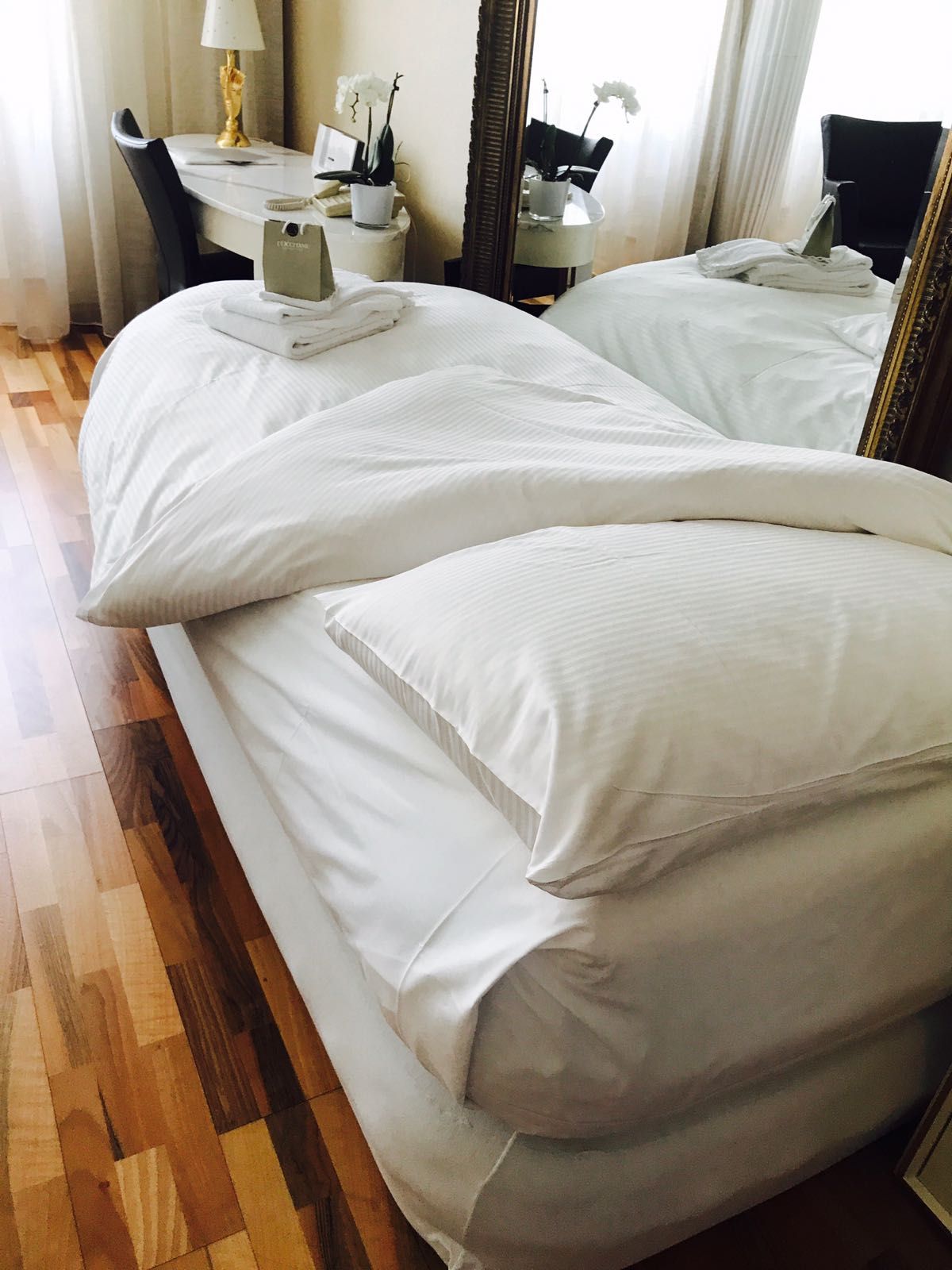 Et hotelværelse med to senge, et skrivebord med lampe, en stol og et spejl.
