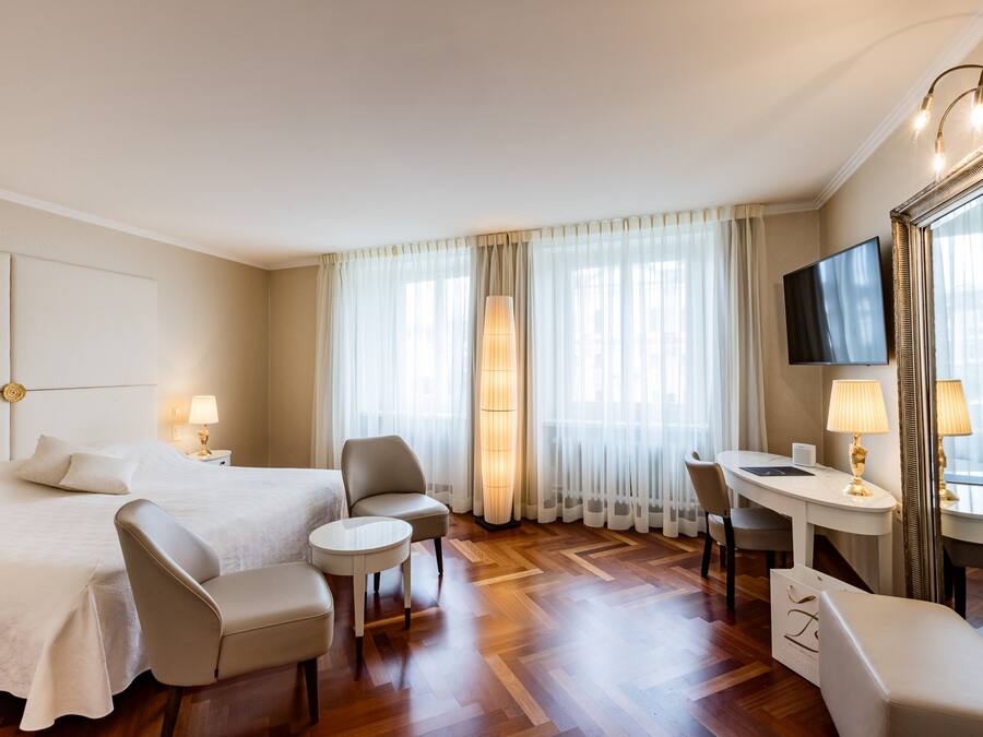 Habitación de hotel con cama, dos sillones, una mesita, escritorio, televisor y un espejo grande.
