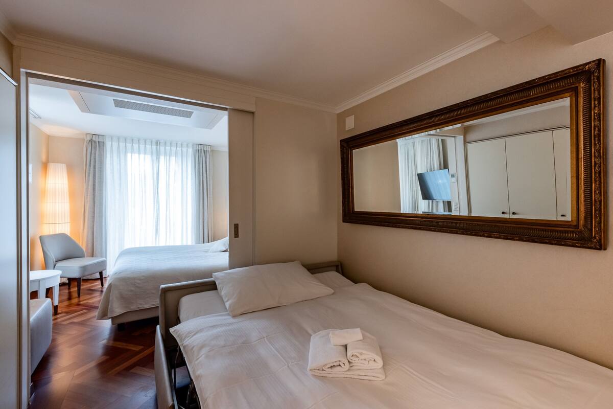 Une chambre d’hôtel avec deux lits, un grand miroir et une vue sur un balcon avec des rideaux.