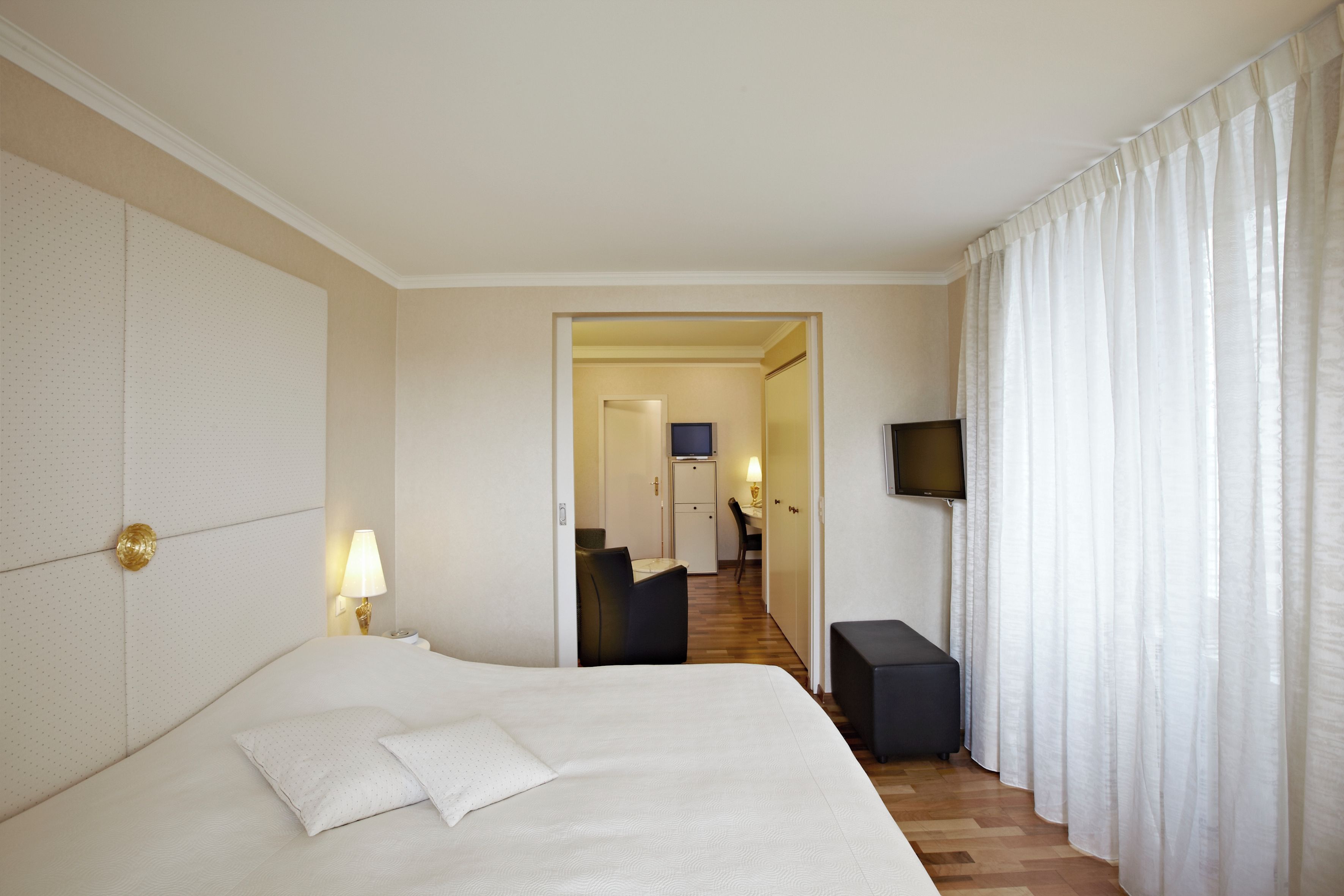 Una habitación de hotel con una cama grande, televisor y vista al pasillo.