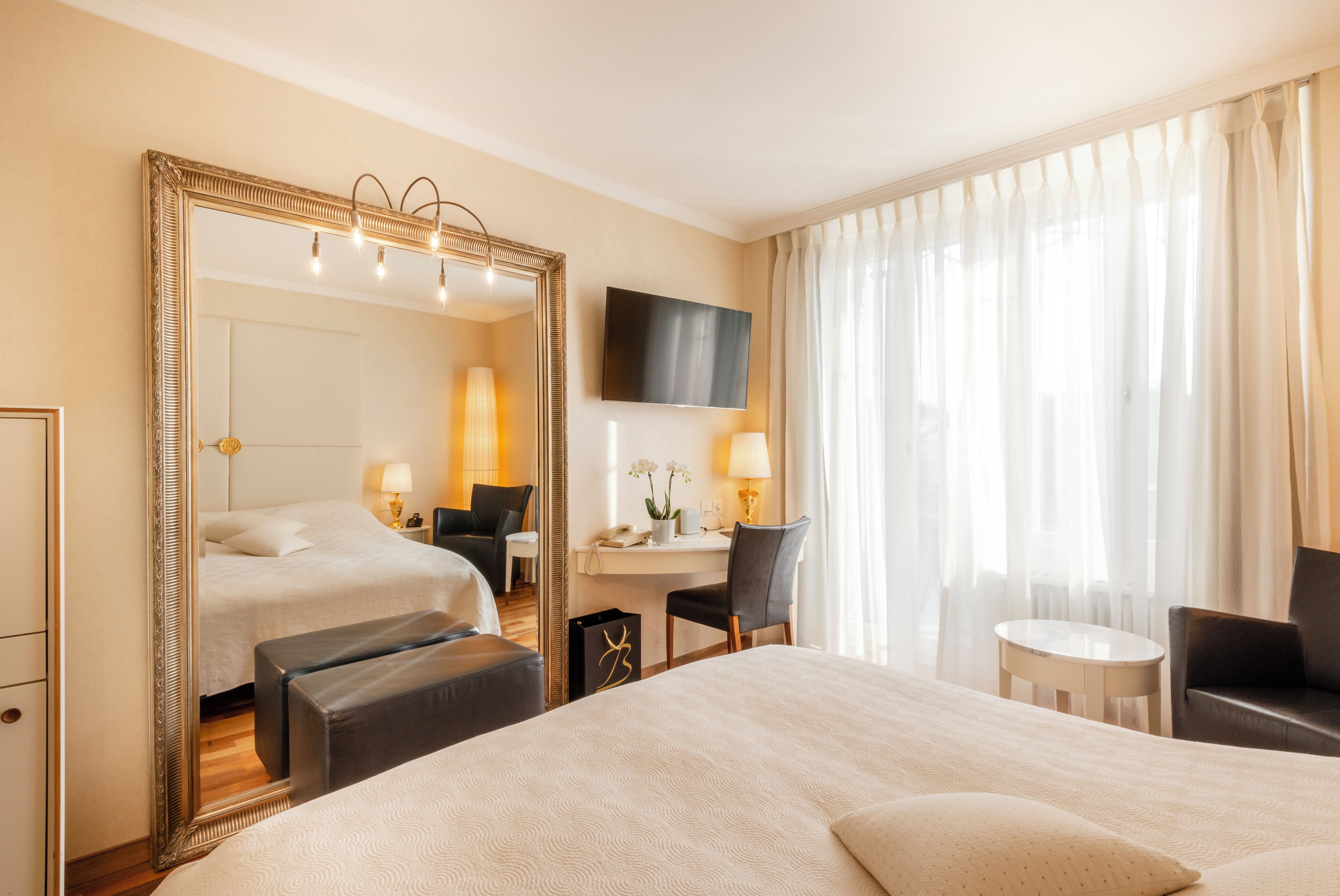 A hotel room with a large bed, a desk, a chair, a small table, and a large mirror.