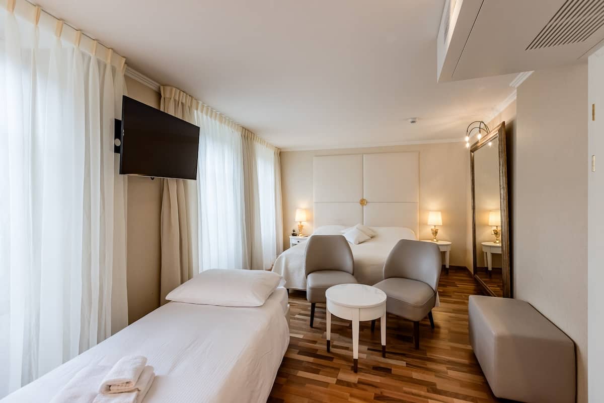 Une chambre d’hôtel comprenant un lit, deux fauteuils, une petite table, un téléviseur et deux lampes de chevet.