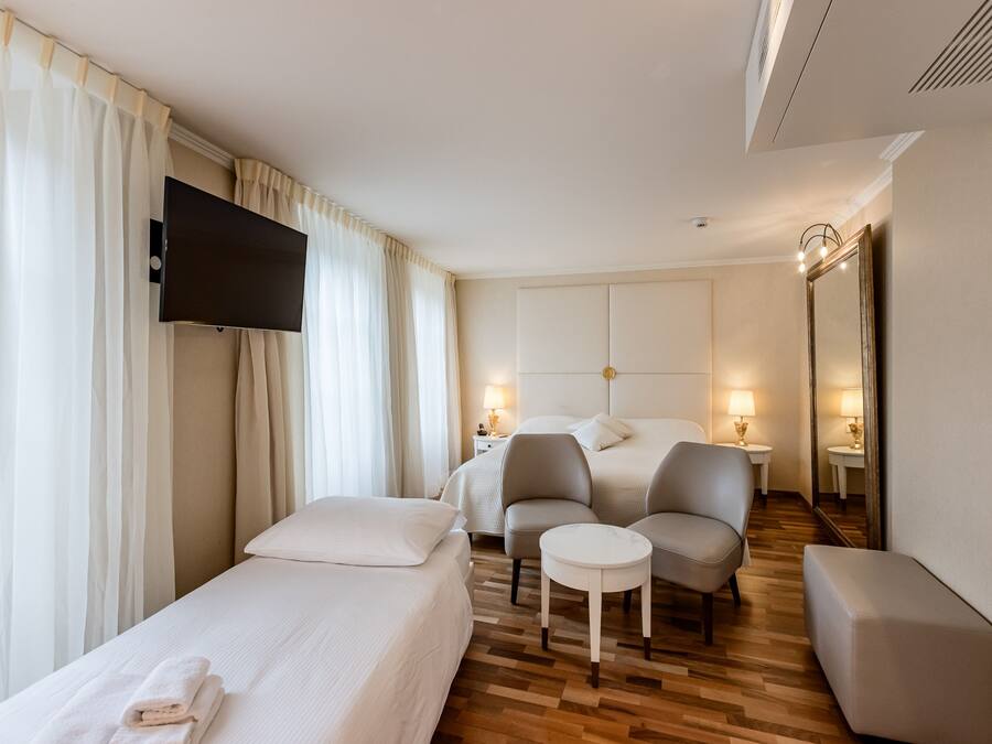 A hotel room with a bed, two armchairs, a small table, a TV, and two bedside lamps.