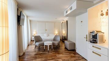 Quarto de hotel com cama, duas poltronas, uma mesinha, televisão, frigobar e espelho.