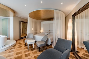 A hotel room with a bed, two chairs, a small table, a bathtub, and a large mirror.