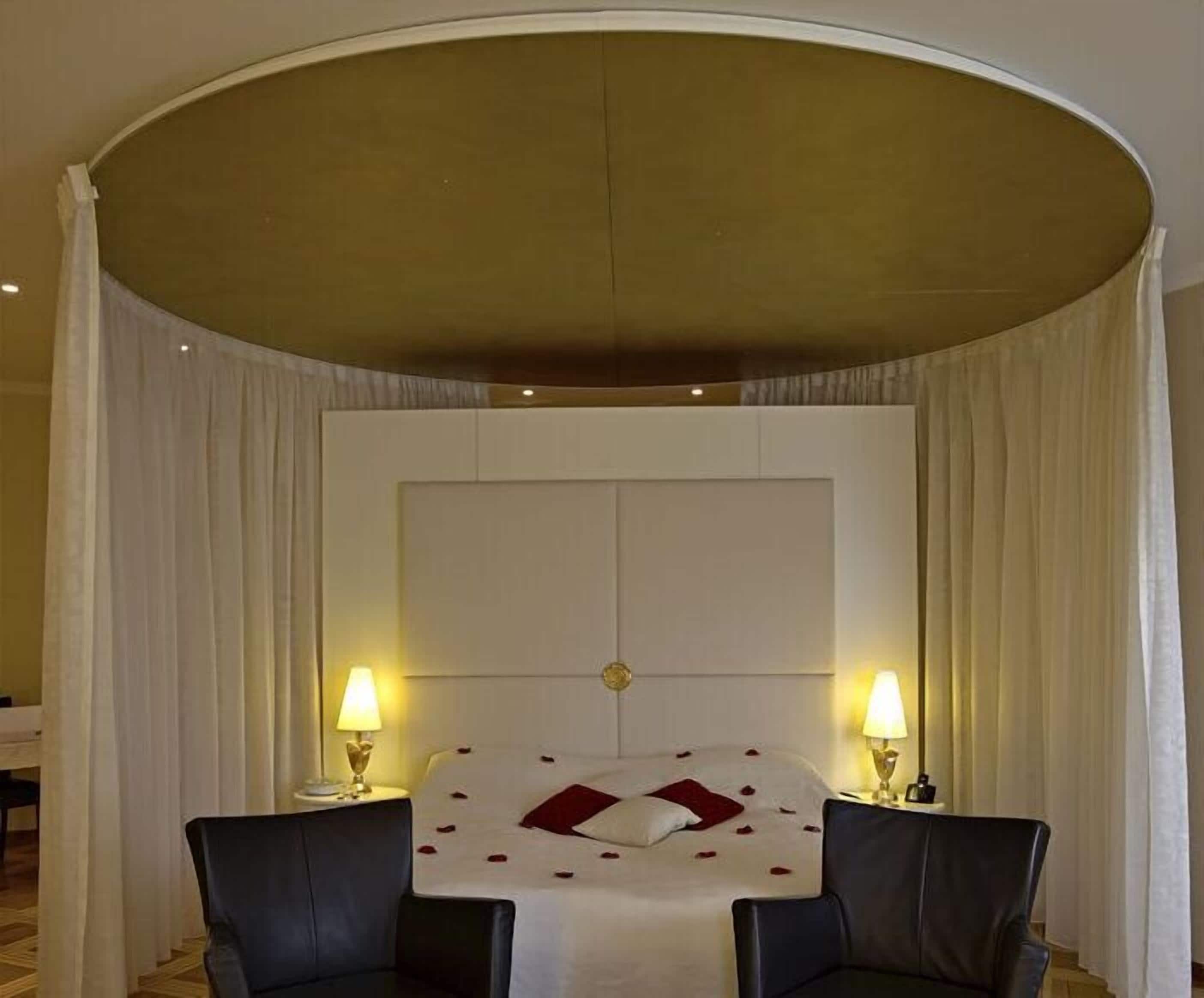 Une chambre d’hôtel avec un grand lit, deux tables de chevet avec des lampes et un plafond cintré.