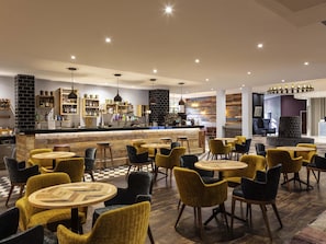 A modern bar area with a counter, seating with round tables and chairs, and a checkered floor. - Novotel Newcastle Airport (Newcastle-upon-Tyne)