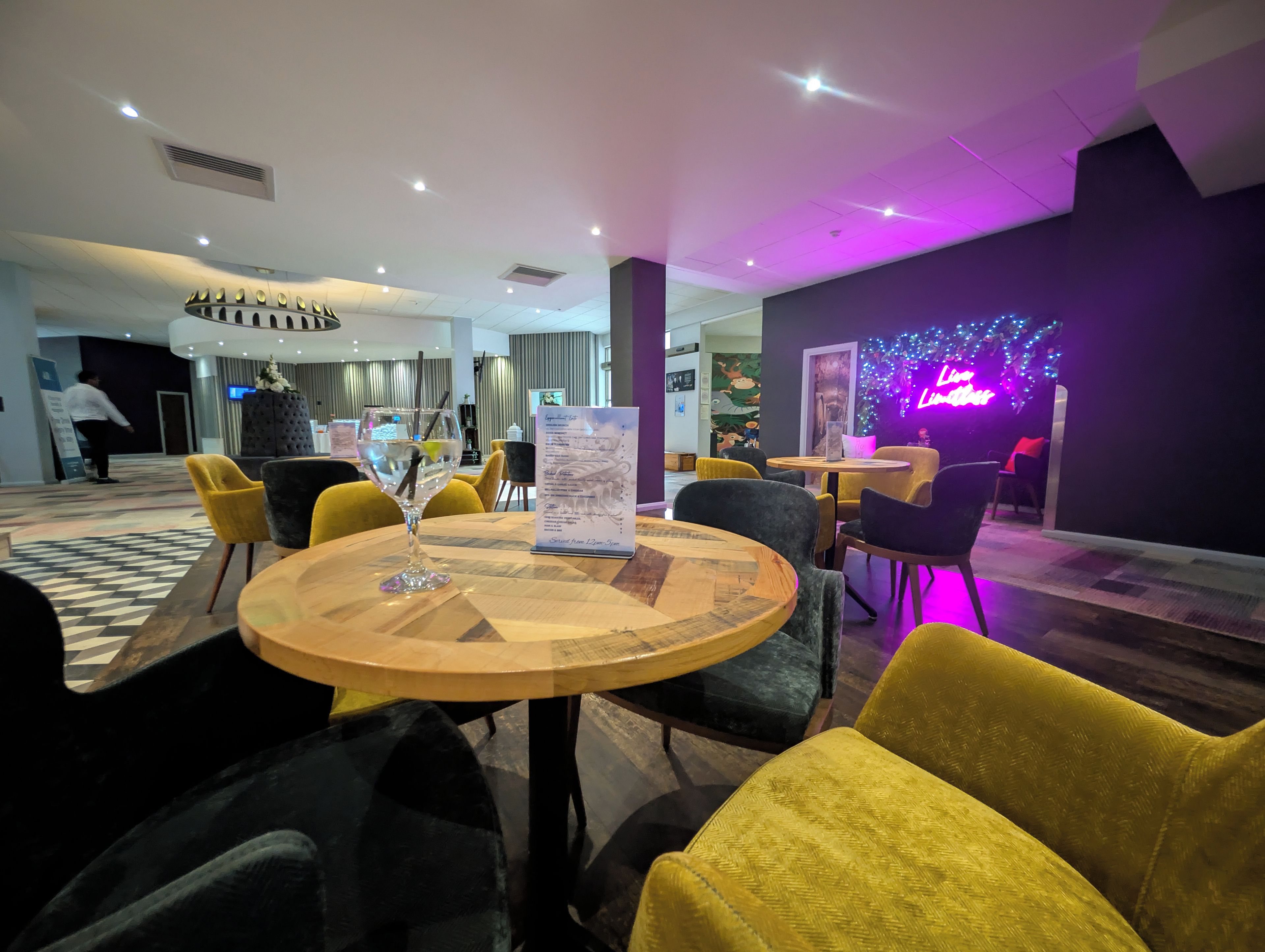 A hotel lobby with round tables, yellow chairs, and a neon sign.