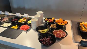 A buffet with various food items including fruits, yogurts, and cooked meats.