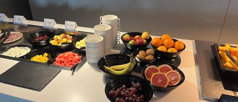 A buffet with various food items including fruits, yogurts, and cooked meats.