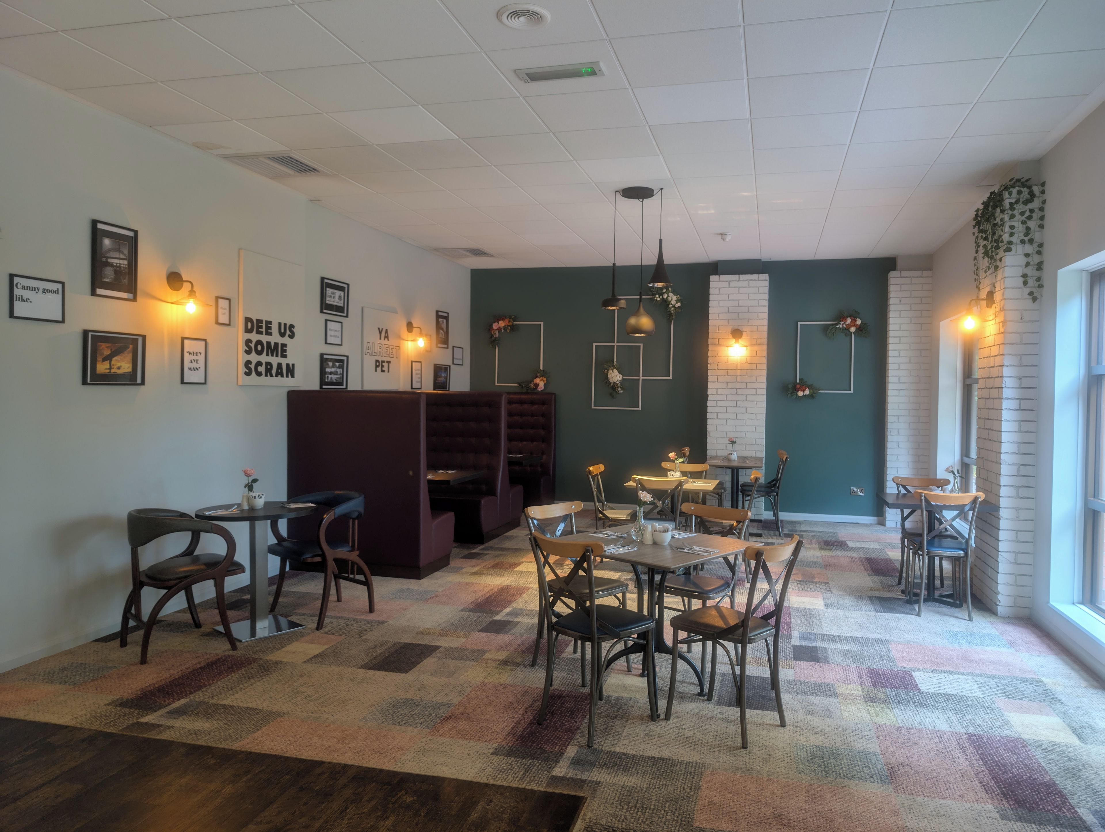 A restaurant interior with booths, tables, and chairs, featuring wall art and pendant lighting.