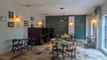 Interior de restaurante con cabinas, mesas y sillas, con obras de arte en las paredes e iluminación colgante.