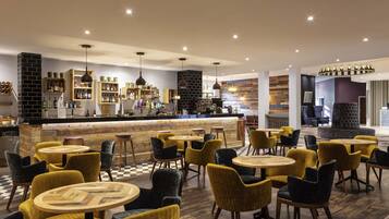 A modern bar area with a counter, seating with round tables and chairs, and a checkered floor.